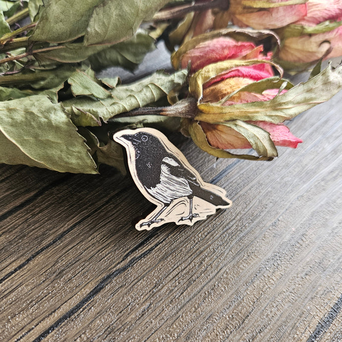 Dried flowers with a magpie wooden badge, on a textured surface